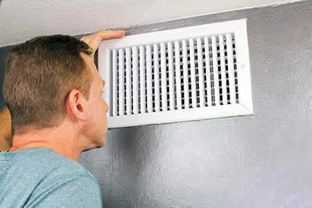 Man looking inside an air vent near the ceiling.