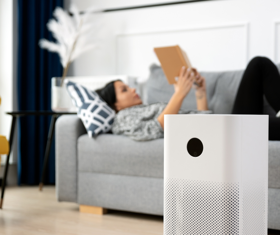 Woman lying on a couch reading, with an air scrubber on the living room floor in foreground.