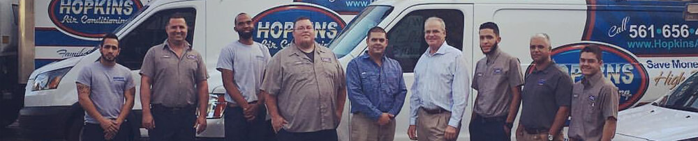 Hopkins Air Conditioning Technicians standing in a row in front of service trucks.