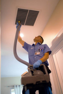 Technician cleaning an HVAC vent in a home's ceiling.