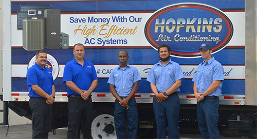 HVAC technicians standing in front of a Hopkins Air Conditioning service truck.