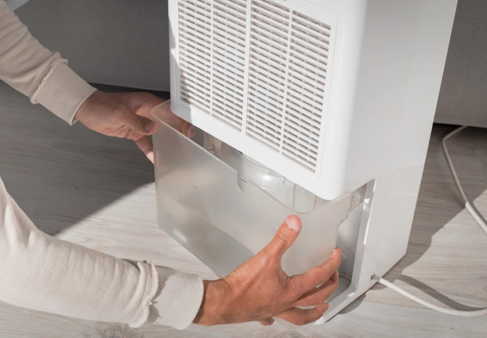 Hands changing a full water bin from a dehumidifier