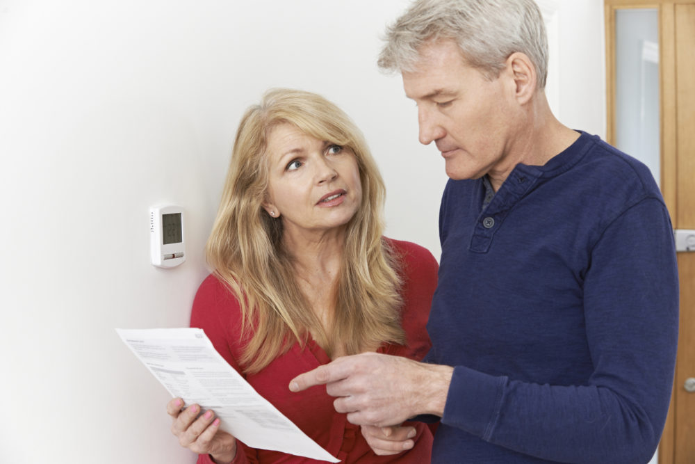 couple by the thermostat looking at an energy bill